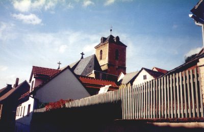 Kirchturm über den Dächern, davor ein Holzzaun