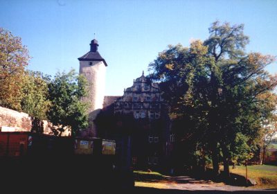 Burgturm und Giebelhaus hinter herbstlichen Bäumen